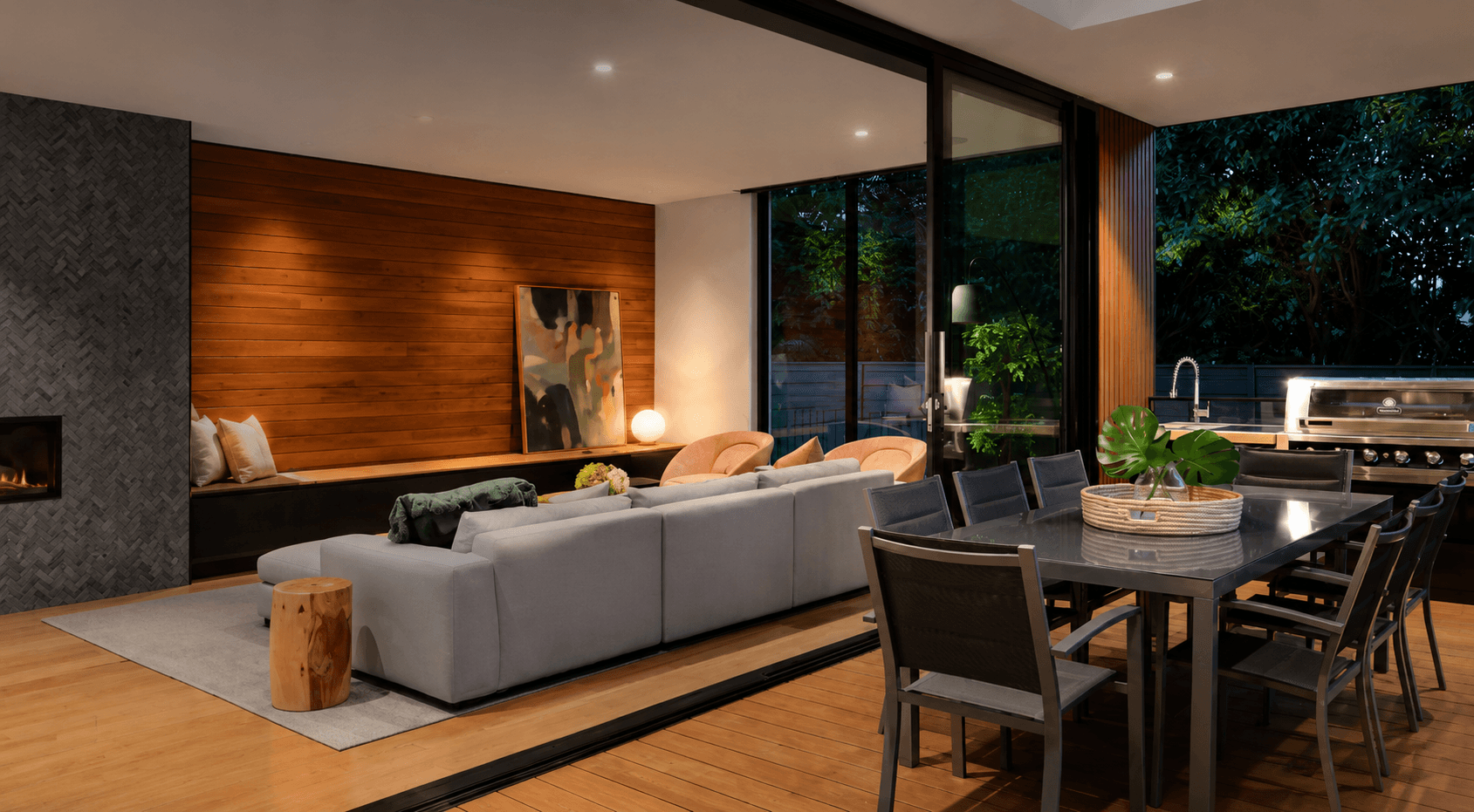 Luxury indoor–outdoor living space at dusk with a warm timber floor, fireplace and designer furniture, the kind of home kept comfortable by underfloor heating