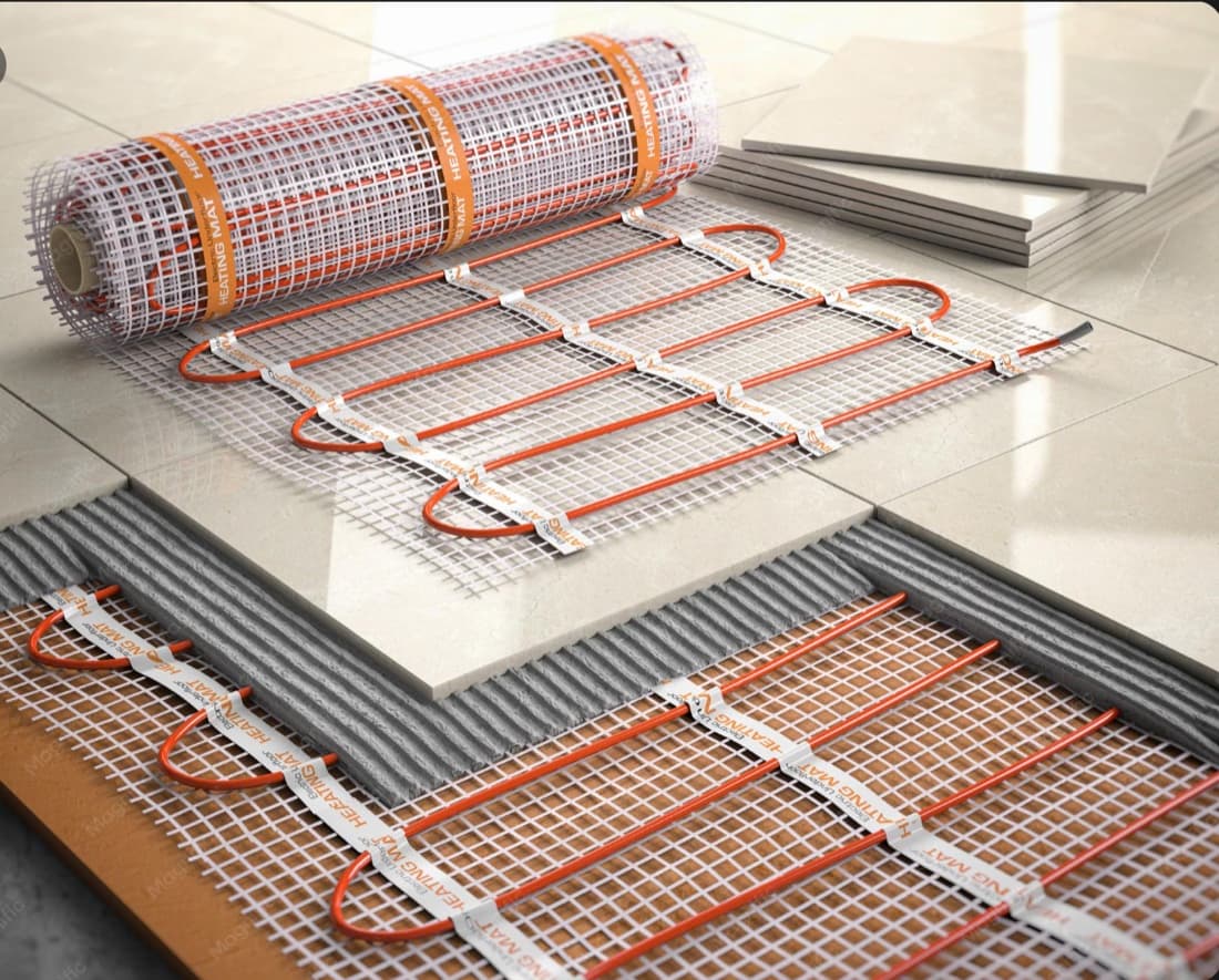 A branded electric underfloor heating mat part-rolled over a tiled floor beside stacked porcelain tiles